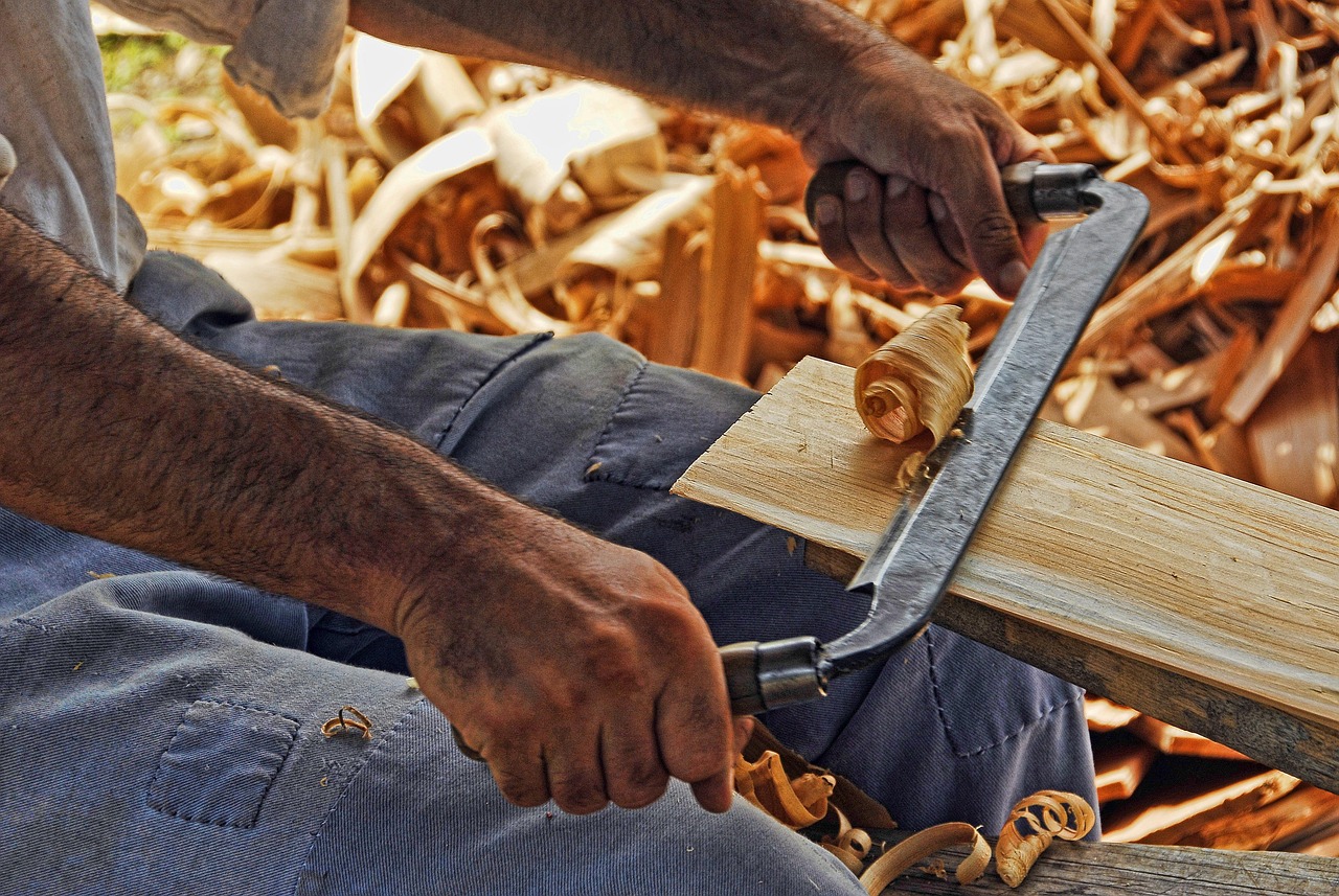 Shaping a leg by hand, with a pile of fresh shavings underfoot.